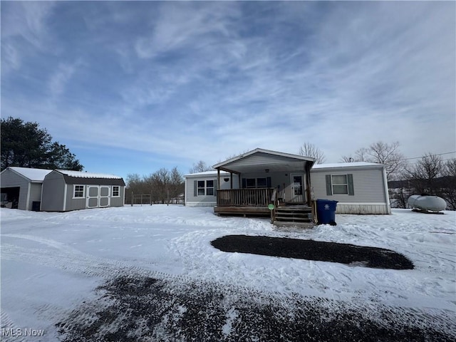 snow covered house with covered porch and a storage shed