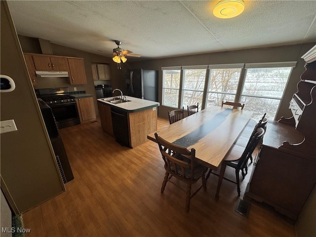 kitchen featuring sink, hardwood / wood-style flooring, a kitchen island with sink, black appliances, and a textured ceiling