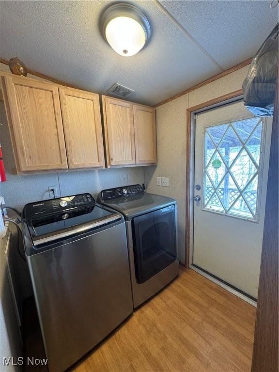 washroom featuring cabinets, a textured ceiling, washer and dryer, and light wood-type flooring