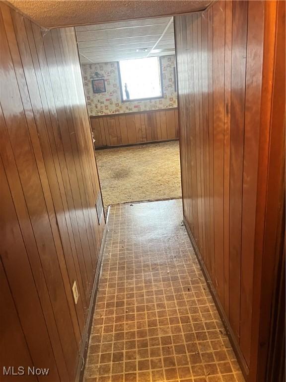 hallway featuring a textured ceiling, carpet, and wooden walls