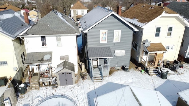 snow covered house featuring central AC unit and a storage unit