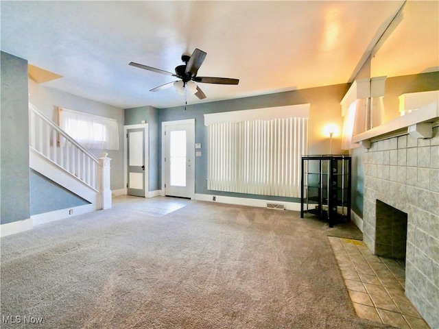 unfurnished living room with carpet, a tiled fireplace, and ceiling fan