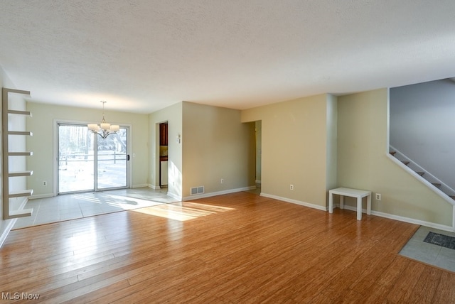 unfurnished living room with a notable chandelier, a textured ceiling, and light hardwood / wood-style flooring