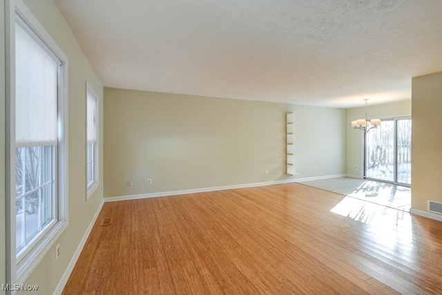 spare room with a textured ceiling, a chandelier, and light hardwood / wood-style flooring