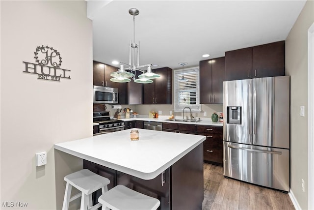 kitchen with light hardwood / wood-style floors, sink, dark brown cabinetry, hanging light fixtures, and stainless steel appliances