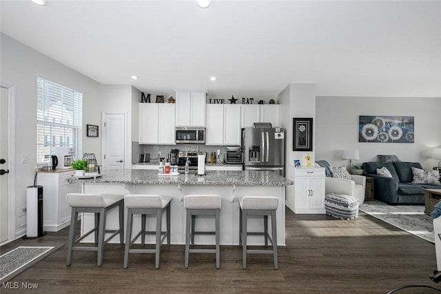 kitchen featuring stainless steel appliances, white cabinets, a breakfast bar, and a kitchen island with sink