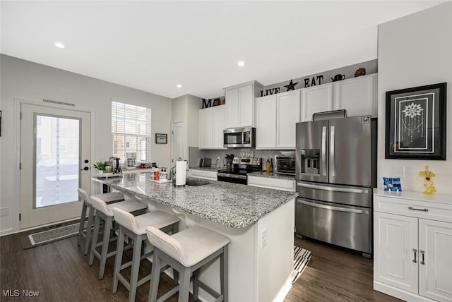 kitchen with white cabinetry, stainless steel appliances, a kitchen breakfast bar, a kitchen island with sink, and light stone counters