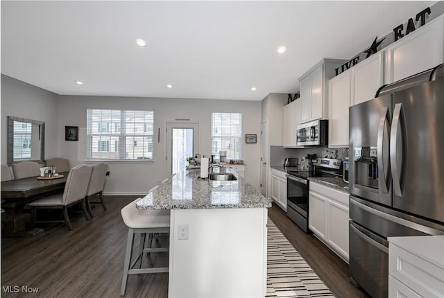 kitchen with a kitchen island with sink, appliances with stainless steel finishes, light stone counters, and white cabinetry