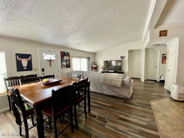 dining space featuring dark wood-type flooring, a textured ceiling, and ornamental molding