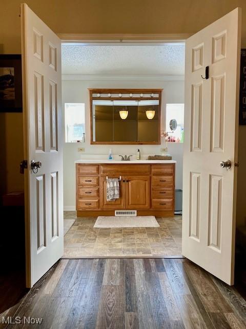 bathroom featuring wood-type flooring, a textured ceiling, vanity, and ornamental molding