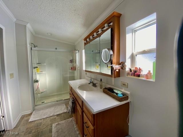 bathroom with vanity, vaulted ceiling, a shower with shower door, a textured ceiling, and ornamental molding