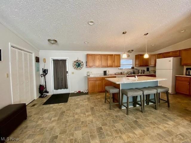 kitchen with white fridge, a center island with sink, a breakfast bar area, decorative light fixtures, and vaulted ceiling