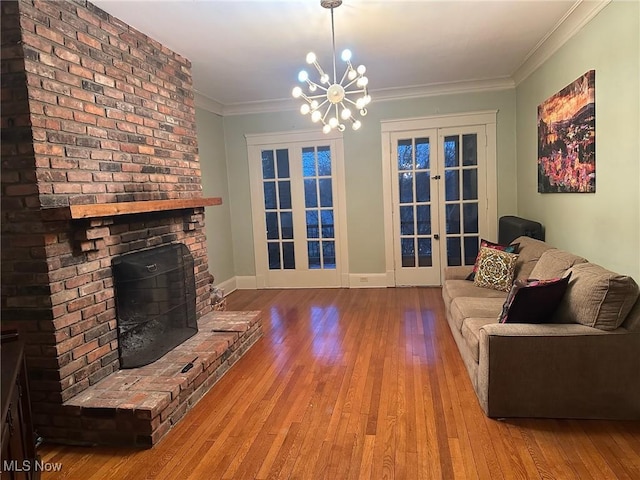 living room featuring hardwood / wood-style floors, a brick fireplace, french doors, a chandelier, and crown molding