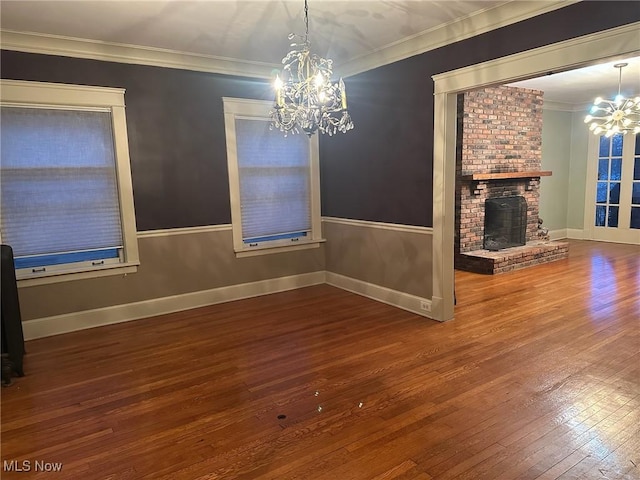 unfurnished dining area featuring a fireplace, a notable chandelier, ornamental molding, and hardwood / wood-style floors