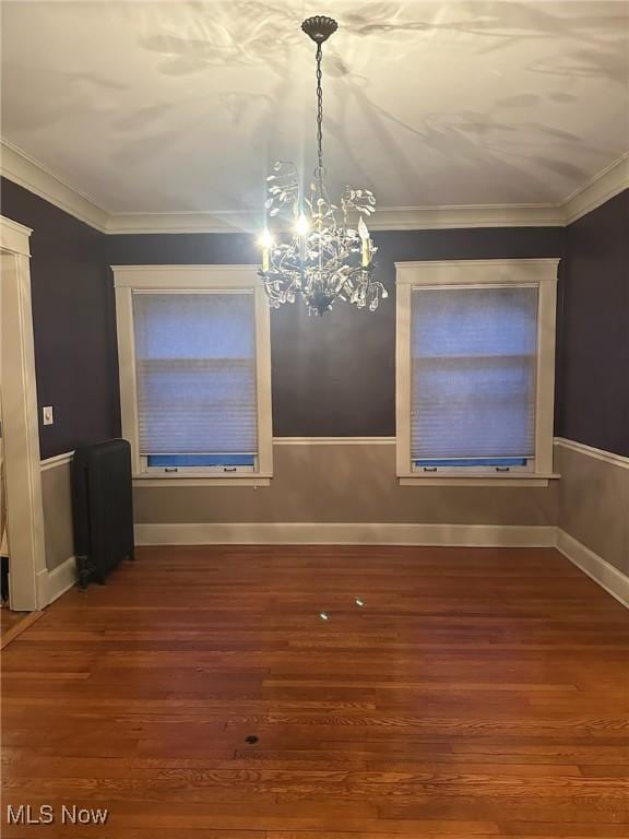 spare room featuring wood-type flooring, radiator, crown molding, and a notable chandelier