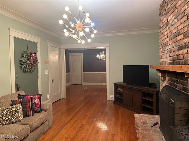 living room featuring a fireplace, wood-type flooring, an inviting chandelier, and crown molding