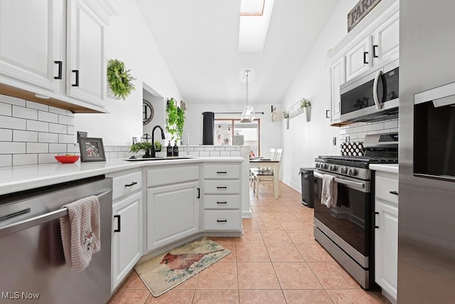 kitchen featuring appliances with stainless steel finishes, vaulted ceiling with skylight, white cabinetry, light tile patterned floors, and kitchen peninsula