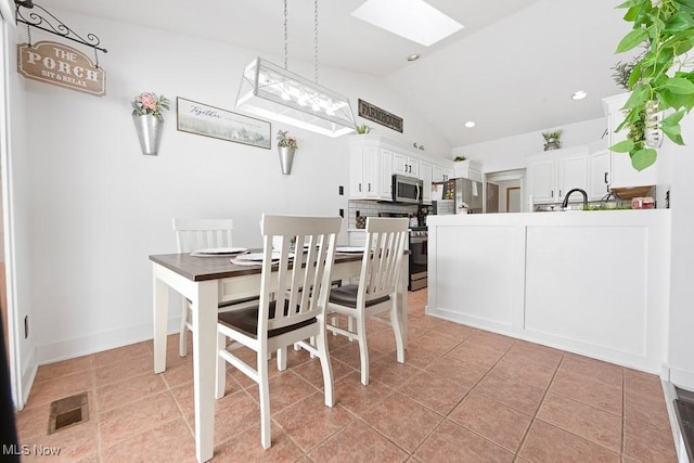 dining area with sink, vaulted ceiling with skylight, and light tile patterned floors