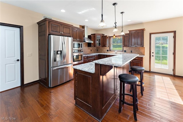 kitchen with light stone countertops, pendant lighting, a center island, stainless steel appliances, and backsplash