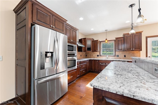 kitchen with wall chimney exhaust hood, stainless steel appliances, tasteful backsplash, hanging light fixtures, and light stone counters