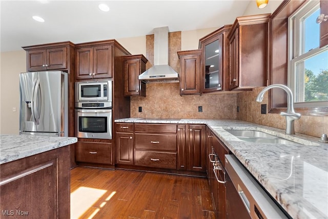 kitchen featuring backsplash, wall chimney range hood, sink, dark wood-type flooring, and appliances with stainless steel finishes