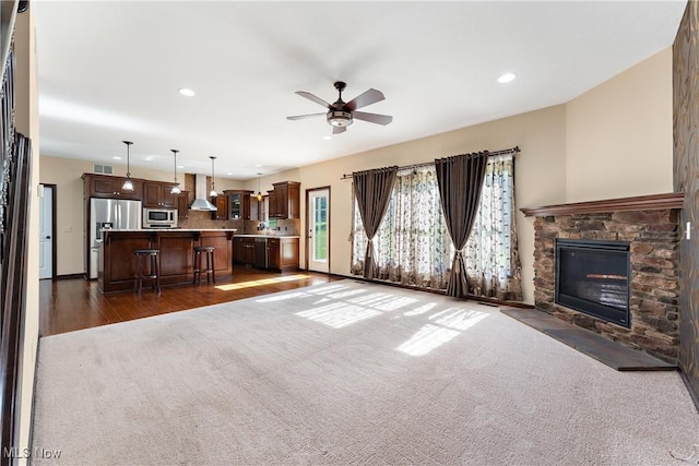 unfurnished living room featuring ceiling fan, a stone fireplace, and dark colored carpet