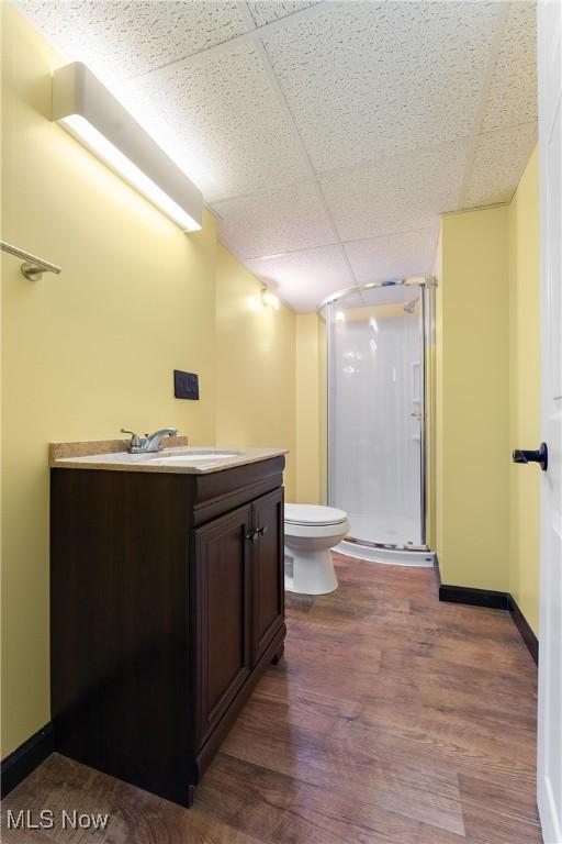 bathroom with toilet, vanity, a drop ceiling, hardwood / wood-style flooring, and a shower with door