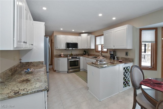 kitchen featuring white cabinets, stone countertops, a peninsula, and stainless steel appliances