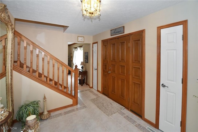 foyer entrance with light tile patterned floors, stairs, baseboards, and a textured ceiling