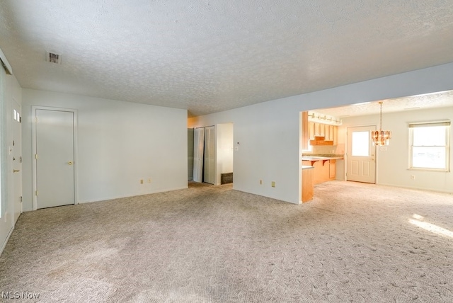 unfurnished living room with light colored carpet, a textured ceiling, and a notable chandelier