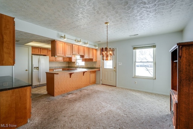 kitchen featuring kitchen peninsula, a breakfast bar area, a healthy amount of sunlight, pendant lighting, and white refrigerator with ice dispenser