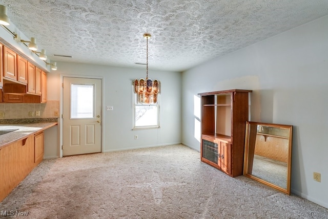 kitchen with tasteful backsplash, light colored carpet, an inviting chandelier, and pendant lighting