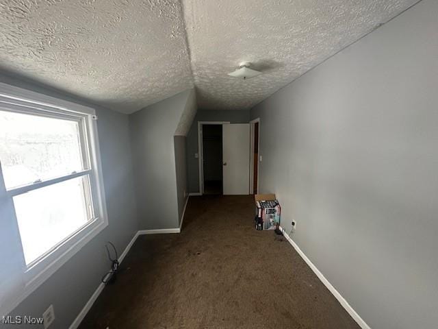 hall featuring dark carpet, plenty of natural light, and a textured ceiling