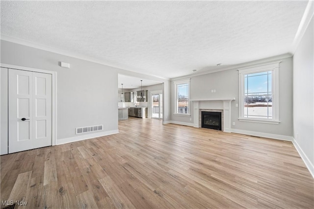 unfurnished living room featuring light hardwood / wood-style floors, a textured ceiling, and crown molding