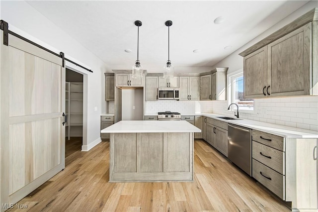 kitchen featuring a barn door, light hardwood / wood-style floors, a kitchen island, hanging light fixtures, and appliances with stainless steel finishes