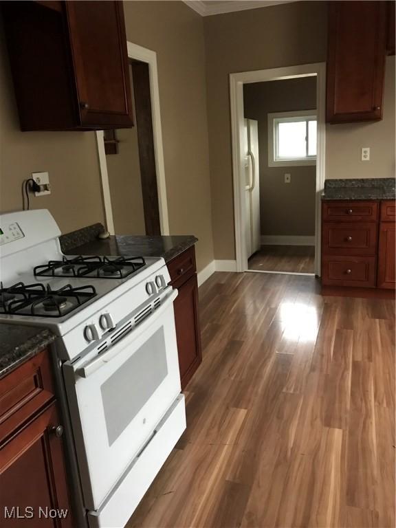 kitchen with dark hardwood / wood-style flooring, dark stone countertops, and white gas range oven