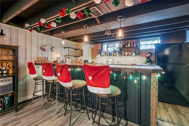 bar featuring black refrigerator, hanging light fixtures, hardwood / wood-style floors, and beamed ceiling