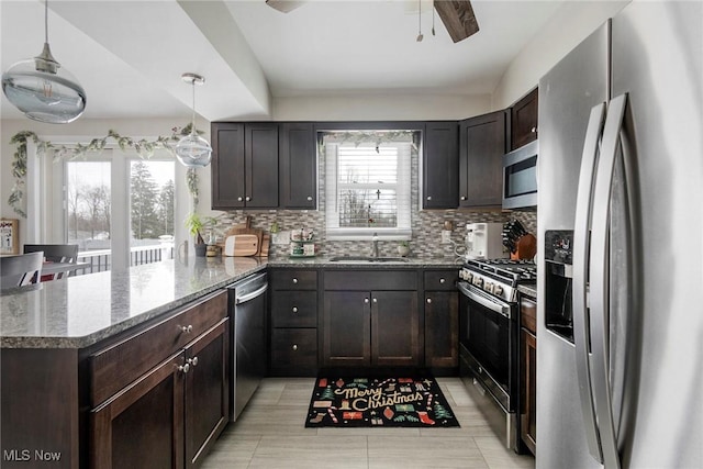 kitchen featuring decorative backsplash, dark stone countertops, hanging light fixtures, and appliances with stainless steel finishes