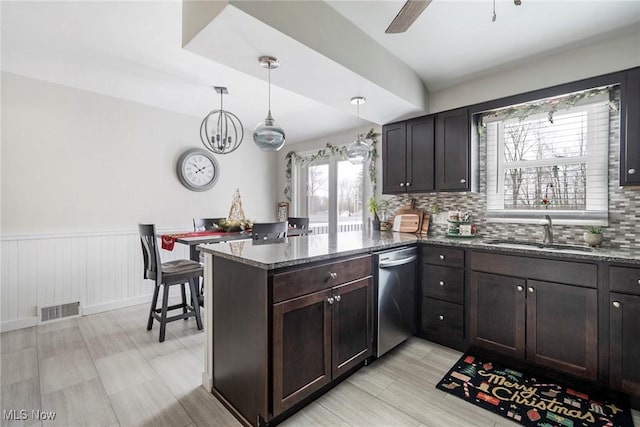 kitchen featuring kitchen peninsula, stainless steel dishwasher, decorative light fixtures, sink, and dark stone countertops