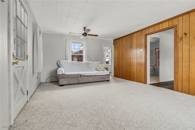 carpeted bedroom with ceiling fan, wood walls, and ornamental molding