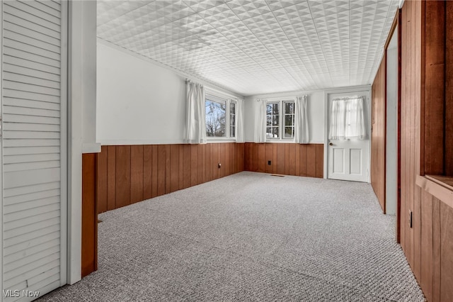 carpeted spare room featuring a wainscoted wall and wooden walls