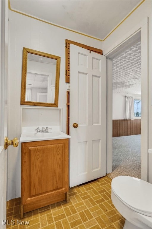 bathroom with wood walls, vanity, brick patterned floor, and toilet