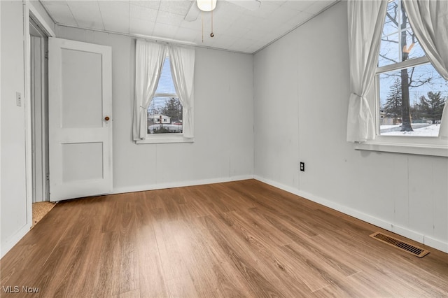 empty room featuring wood finished floors, visible vents, a ceiling fan, and a healthy amount of sunlight