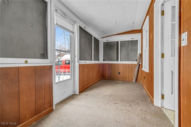 interior space with carpet floors, lofted ceiling, wooden walls, and plenty of natural light