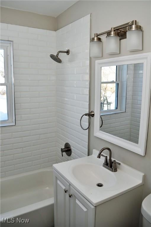 full bathroom featuring a wealth of natural light, toilet, vanity, and tiled shower / bath