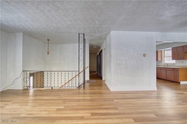 empty room with sink, a textured ceiling, and light wood-type flooring