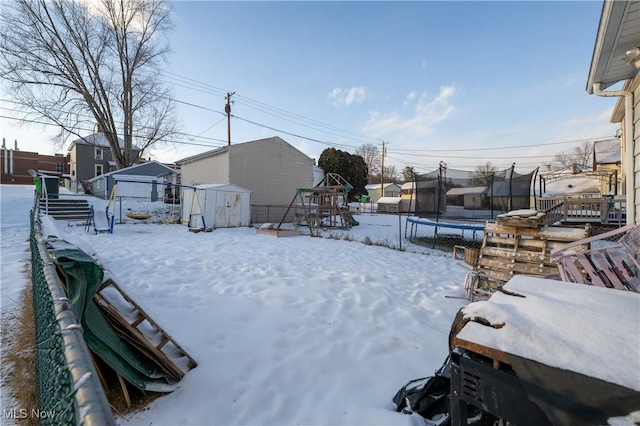 yard layered in snow with a storage unit and a trampoline