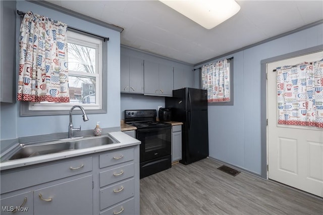 kitchen featuring black appliances, gray cabinetry, sink, light hardwood / wood-style flooring, and ornamental molding