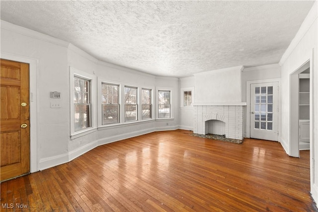 unfurnished living room featuring a brick fireplace, wood-type flooring, ornamental molding, and a textured ceiling