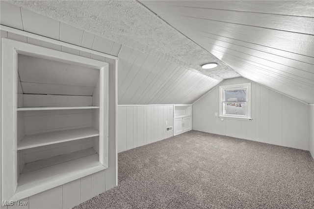 additional living space featuring carpet floors, a textured ceiling, lofted ceiling, and wooden walls